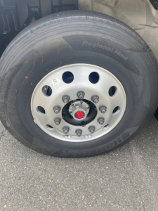 Truck wheel close-up showing a silver steel rim with multiple lug nuts and a red center cap, tire labeled 'Regional Haul' on the sidewall.