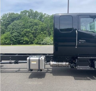 Truck cab chassis side view showing fuel tank and exhaust/bracket assembly along the frame.