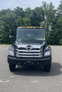 Front view of a new 2027 Hino L7 cab chassis truck showing bold chrome grille, Hino emblem, rectangular headlights, and amber cab roof lights.