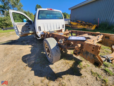 GMC Sierra 3500HD cab and chassis with open doors, exposed rusty frame, and front wheel visible; yard setting.