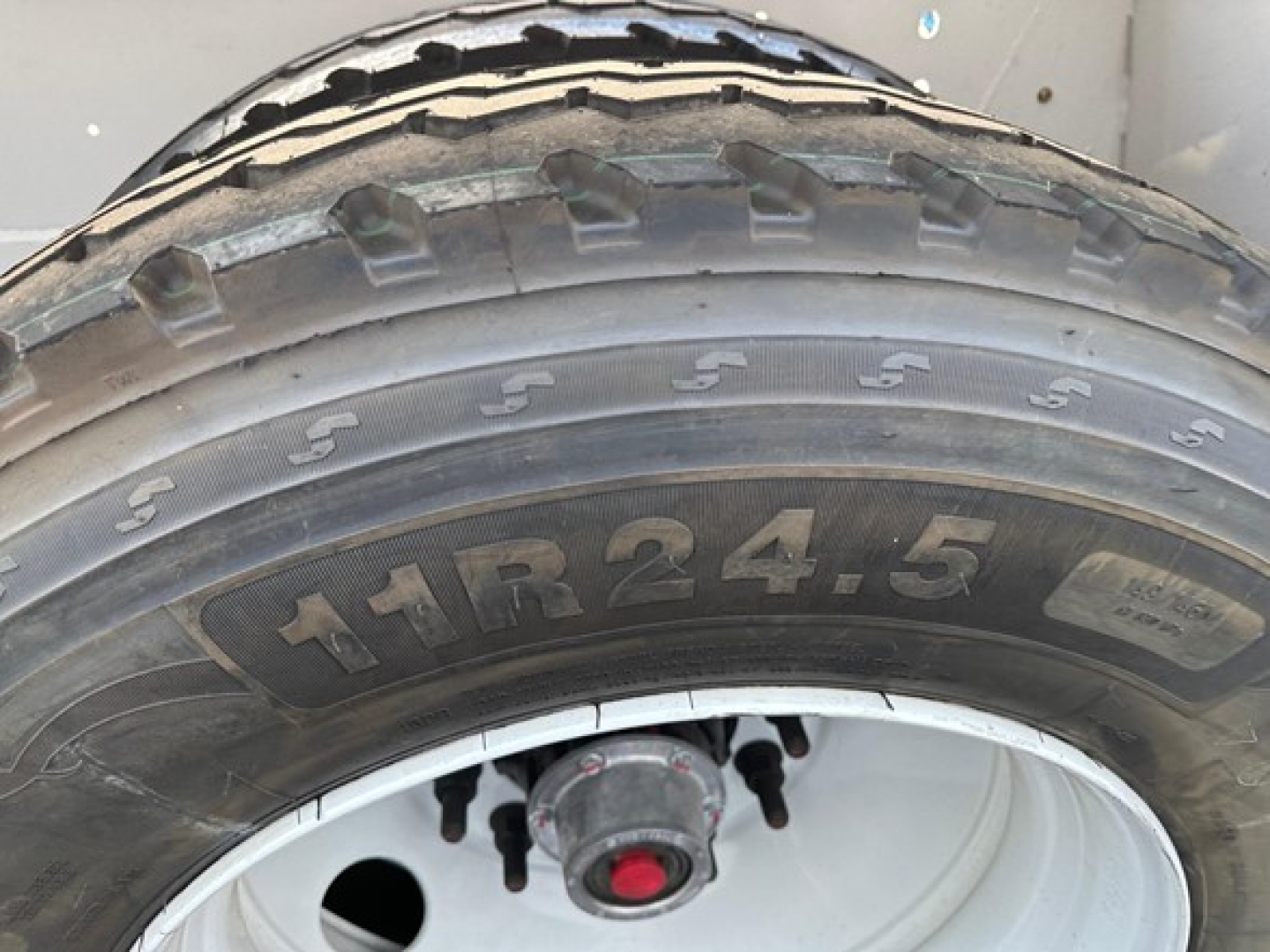 Tire with visible tire markings '11R24.5' and wheel hub area; portion of frame and trailer components visible.