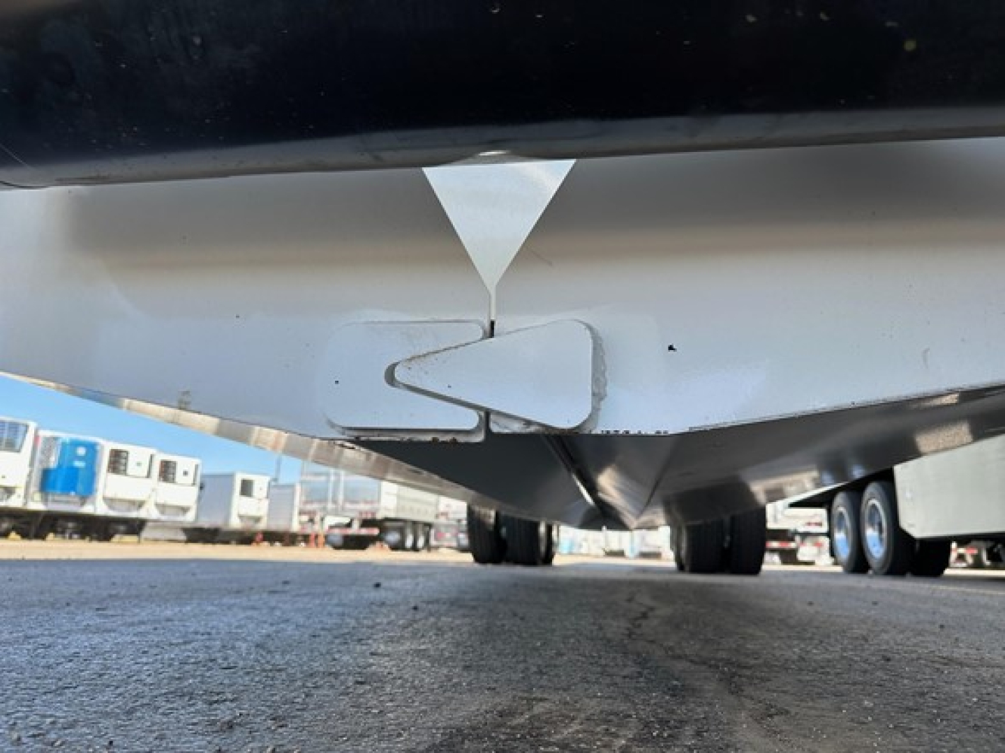 Bottom dump trailer underside with warning and hinge area visible, showing light gray metal and underside details.