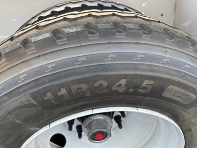 Tire with visible tire markings '11R24.5' and wheel hub area; portion of frame and trailer components visible.