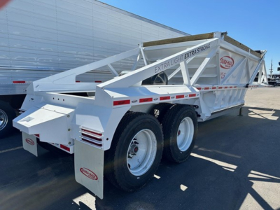 Bottom dump trailer with white frame and dual rear axles showing “EXTRA LIGHT EXTRA STRONG” along side; large side trough; brand badge on rear; tire rims visible.