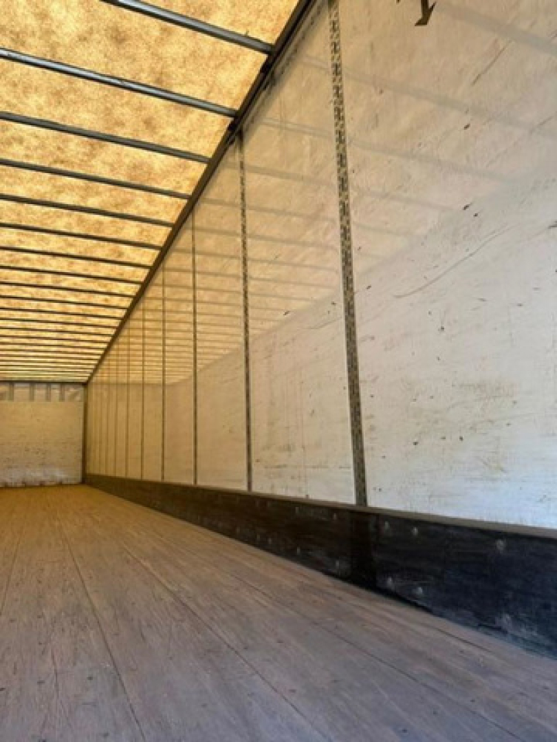 Trailer interior showing empty cargo area with wooden floor and white side walls and overhead ribs.