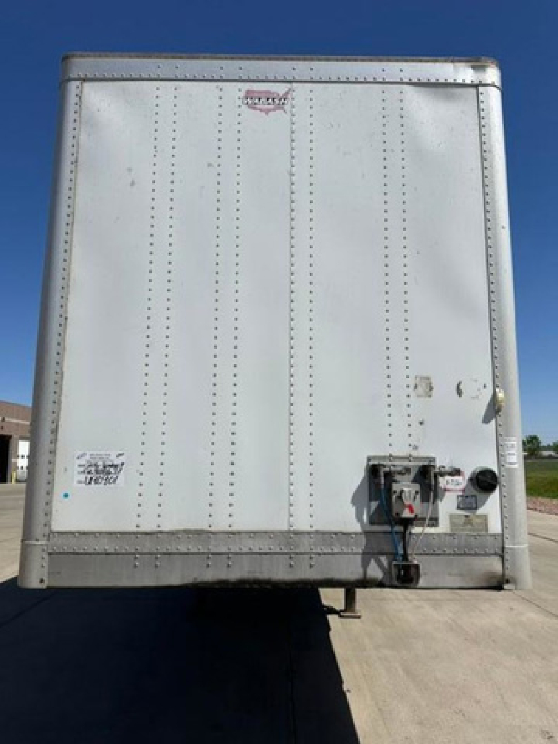 Rear view of a white Wabash van trailer with vertical riveted panels and a small door hardware at the bottom right, no visible branding legible