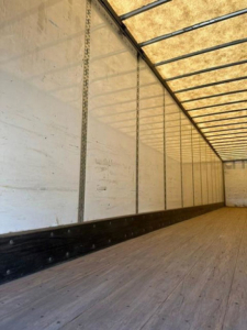 Interior of a Wabash van trailer showing wooden floor and white sidewalls with a black lower trim; no legible labels visible.