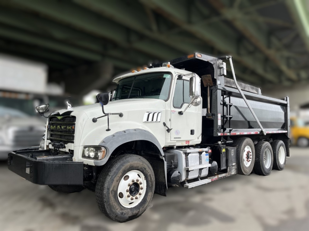 Mack GR84F dump truck with white cab under bridge showing front bumper and air intake.