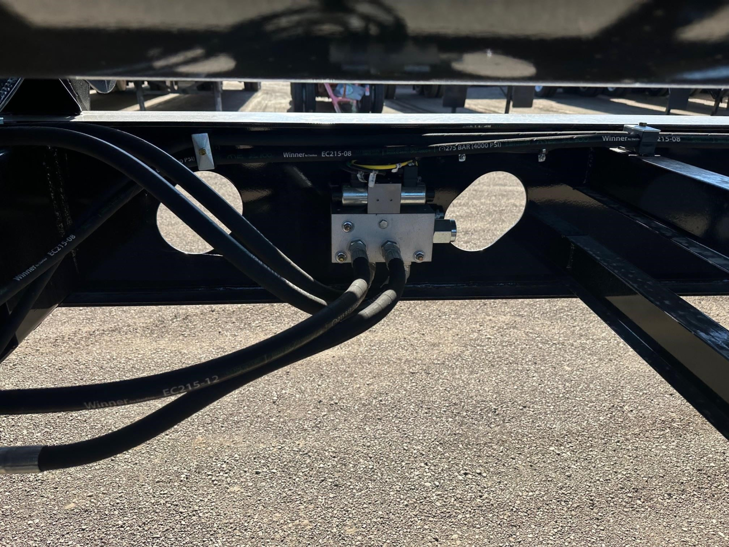 Trailer underside showing hydraulic hoses connected to a metal junction block on a dump trailer frame.