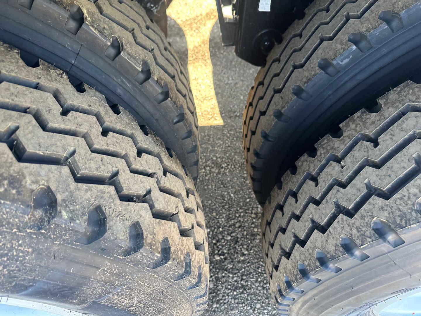 Tandem trailer tires in a close-up view of a dump trailer undercarriage showing tire treads and black wheel hubs.