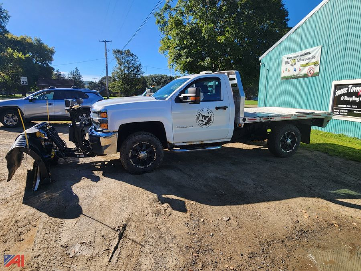 Chevrolet Silverado 3500HD flatbed truck with plow attachment in front, white cab, black wheels, side logo, daytime outdoor setting