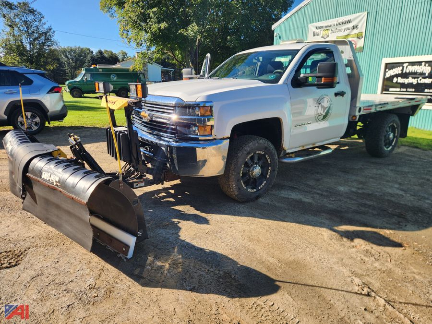 Chevrolet Silverado 3500HD flatbed truck with front plow attachment, white cab, green utility bed, visible chevrolet emblem, daytime outdoor lot.