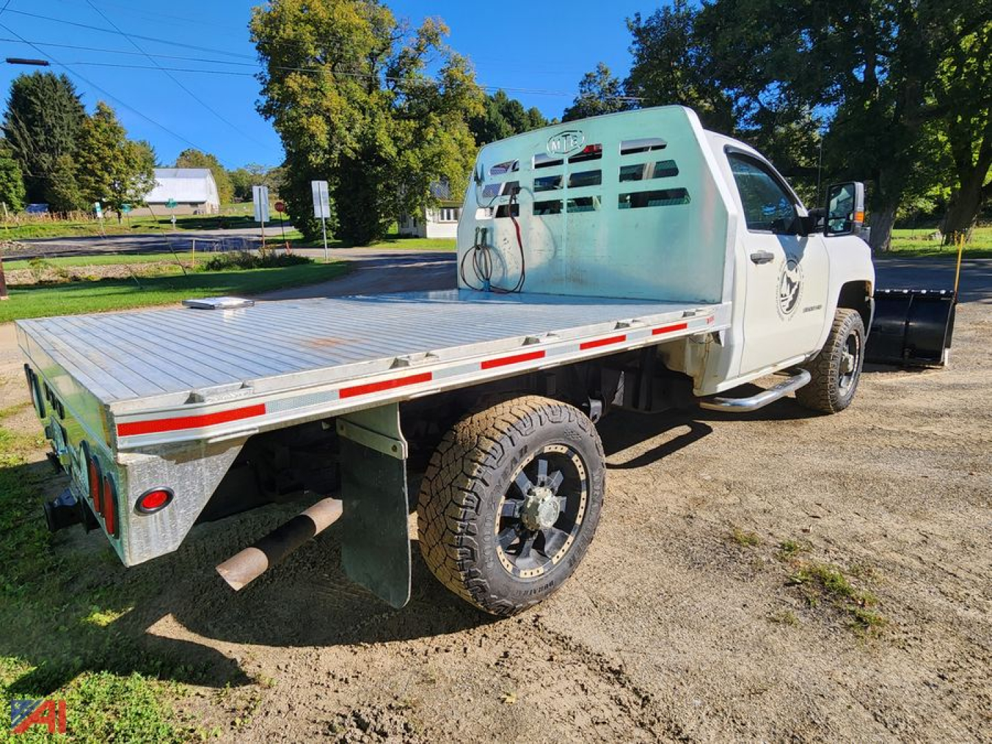 Flatbed truck with plow and aluminum bed showing rear and side profile; white cab, heavy-duty dual-wheel rear, spare tire, and bumper; VIN plate not visible.