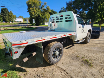 Flatbed truck with plow and aluminum bed showing rear and side profile; white cab, heavy-duty dual-wheel rear, spare tire, and bumper; VIN plate not visible.