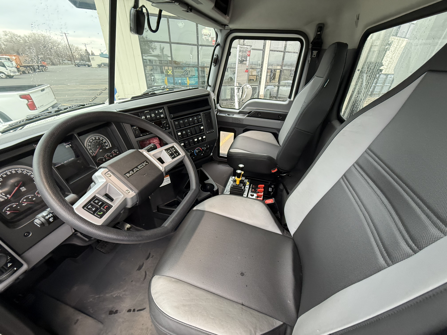 Truck cab interior of a 2025 Mack GR104F showing steering wheel, dashboard, and front seats with center console and gear shifter.