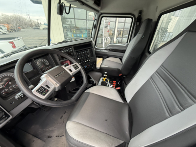 Truck cab interior of a 2025 Mack GR104F showing steering wheel, dashboard, and front seats with center console and gear shifter.