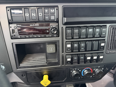 Mack GR104F dash view showing gear selector R N D M with drive mode, radio unit labeled MACK, row of switches, climate controls, and a yellow parking brake/air valve knob.