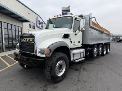 Mack GR104F dump truck in white with chrome grille, front bumper, and orange dump bed side rails, shown in a dealership lot.