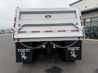Dump truck bed rear showing OSW Equipment & Repair, LLC mud flaps, taillights, chains, and rear hydraulic connections on a Mack GR104F with a silver dump body.