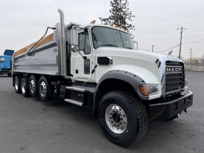 Mack GR104F dump truck side/front view showing large chrome grille, white cab, multi-axle chrome wheels, dump bed, and side steps.