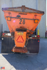 Rear view of a used 1985 Ford L8000 stone/spreader truck with orange hopper, number 28, rear hazard triangle, and trailer hitch, in-service condition.