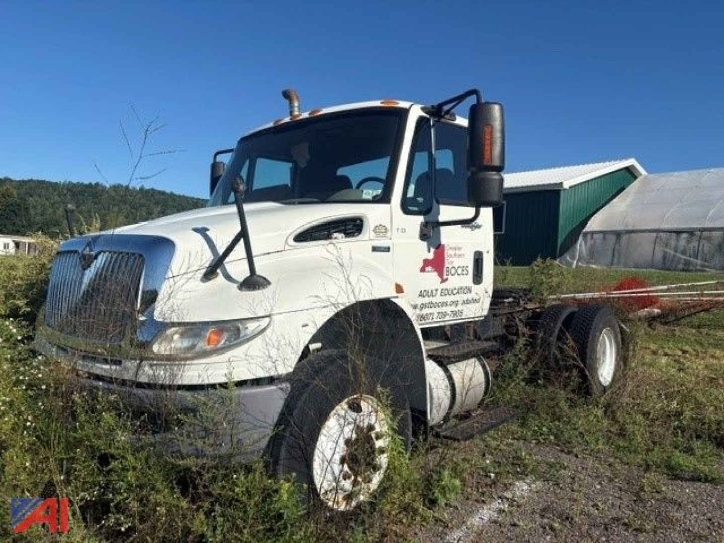 Truck cab exterior with International DuraStar 4400 chassis, white daycab, large grille, side mirrors, and fuel tanks. Visible text on door includes company logo and contact info, but small and not fully legible.