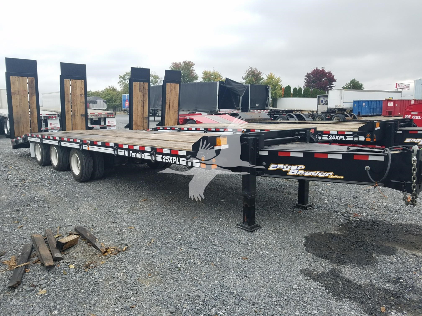 Trailer showing low-profile gooseneck flatbed with wood-sided ramps and dual tandem axles, visible brand 'Eager Beaver' and model '25XPL' labels.