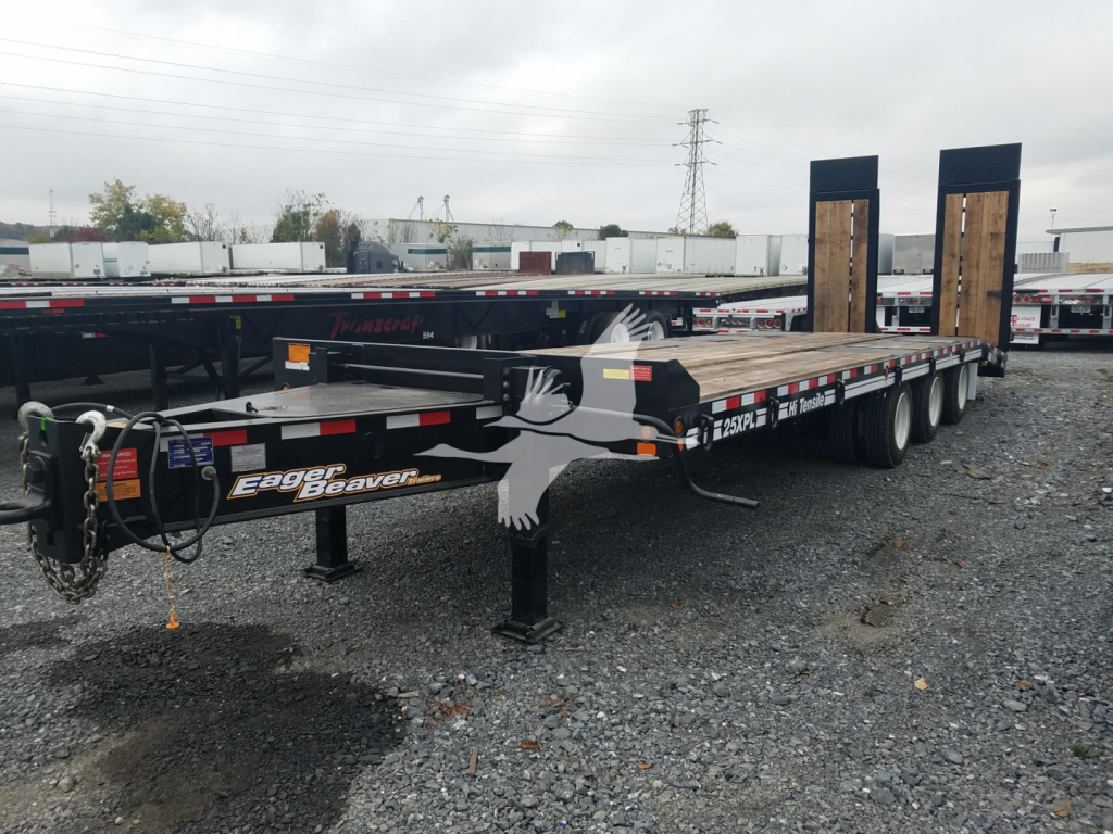 Trailer with dual rear ramps and long flatbed, featuring Eager Beaver branding and a chain, parked on gravel.
