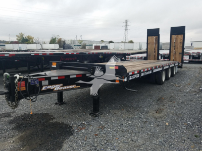 Trailer with dual rear ramps and long flatbed, featuring Eager Beaver branding and a chain, parked on gravel.