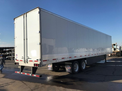 Trailer side view showing large rectangular white utility trailer with dual rear doors and undercarriage wheels.