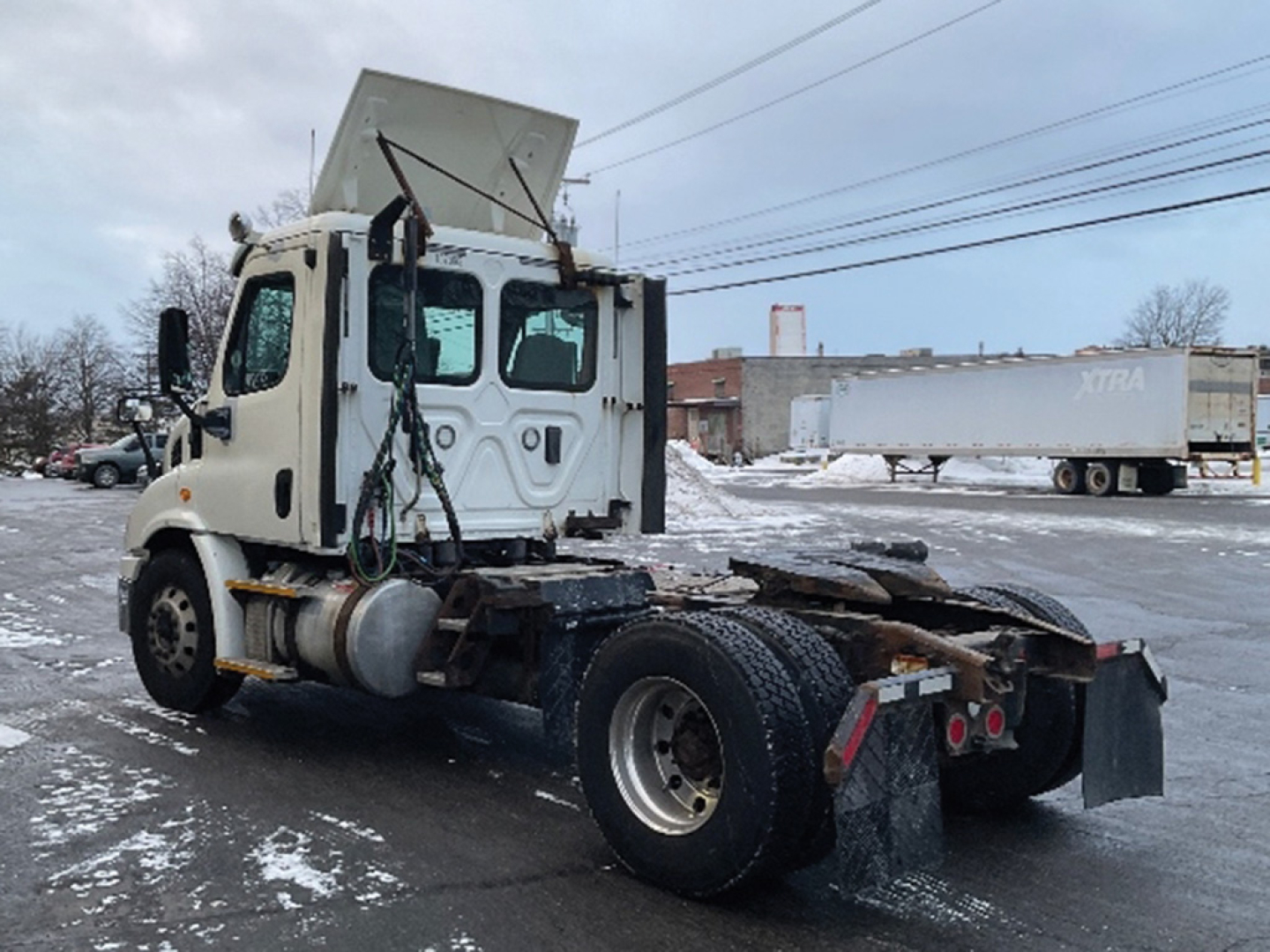 Medium shot of a white Freightliner Cascadia113 daycab chassis without a cab; visible wheelbase with dual rear axles and exposed frame, truck bed area, snow on ground; no cargo.