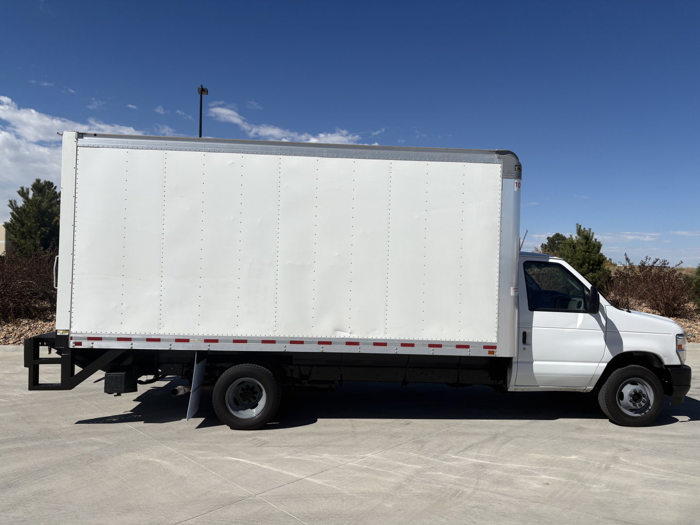 Box truck side view showing large white cargo box on a Ford E350 chassis with cab in front, stock number 0633464 and VIN visible in listing.