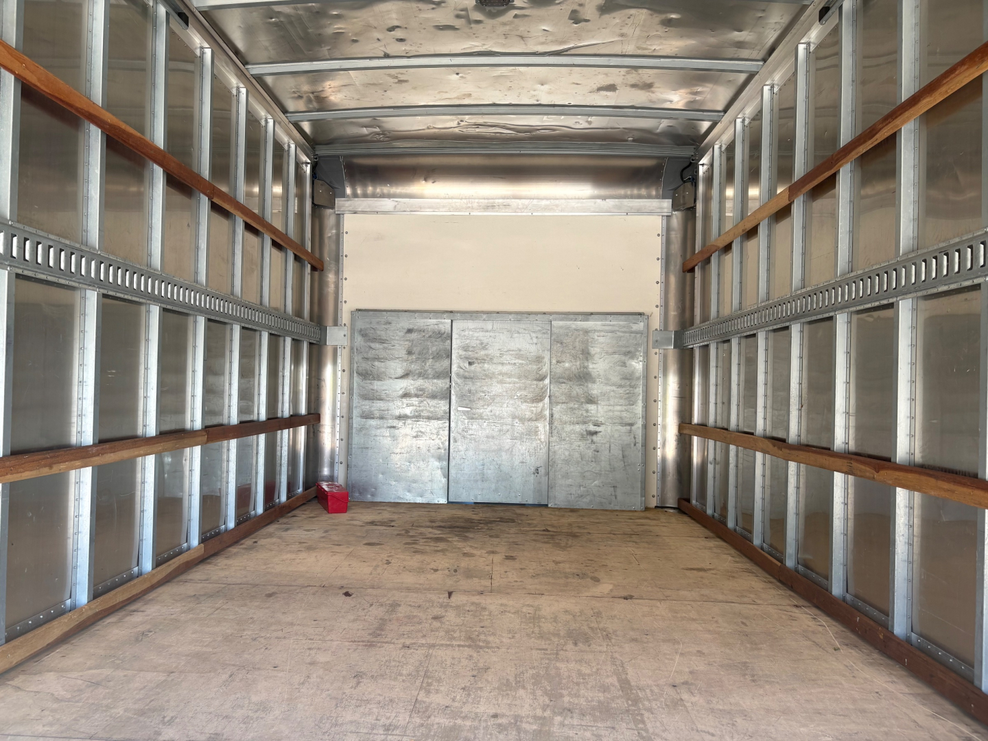 Box truck cargo area showing empty metal walls with wooden siderails and rear metal doors.