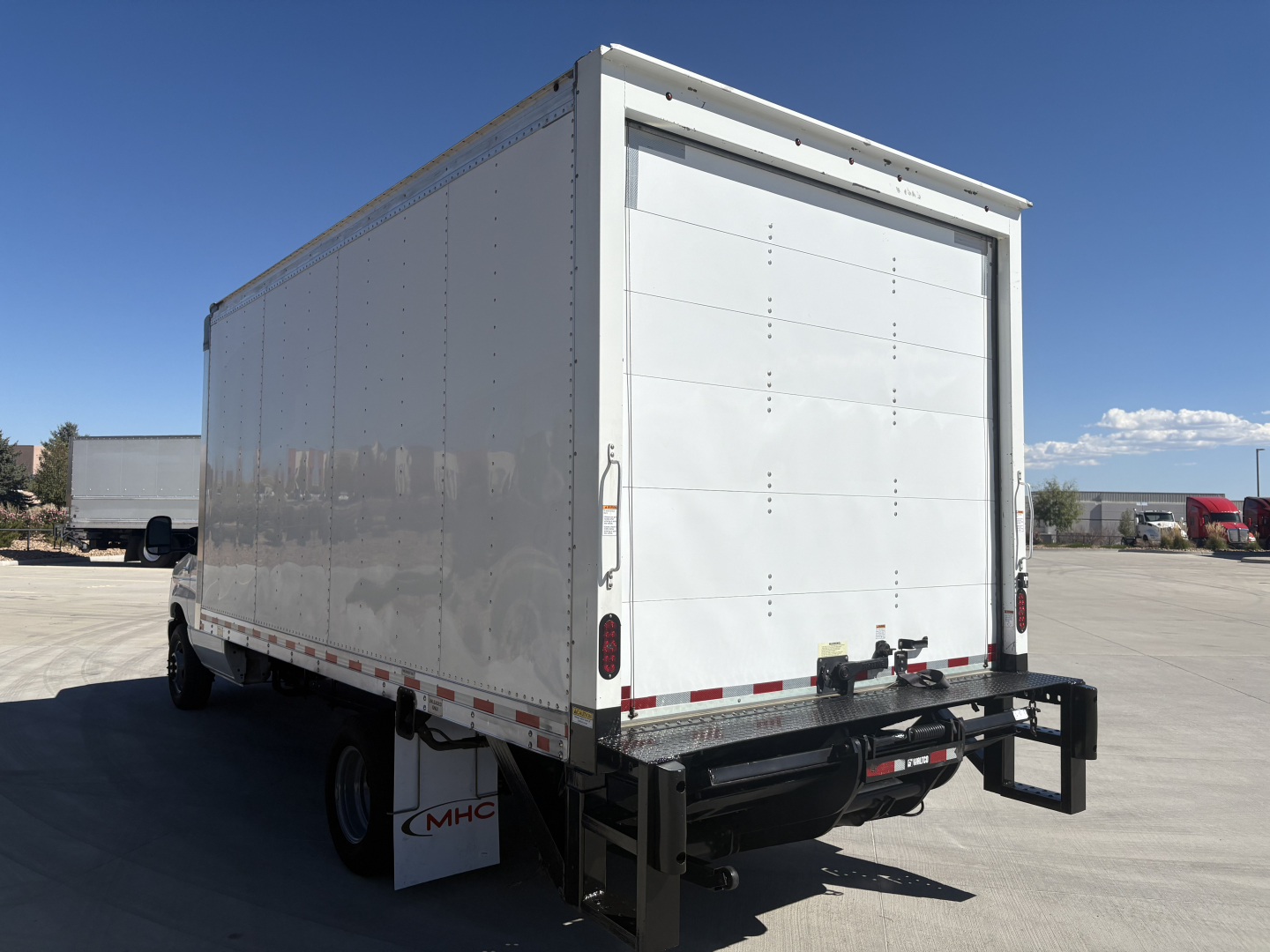 Box truck rear view showing large white cargo box, Ford E350, rear doors, bumper, taillights, and black hitch with safety chains. No visible text besides general vehicle features.