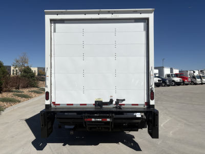 Rear view of a white box truck with liftgate on a dealership lot.