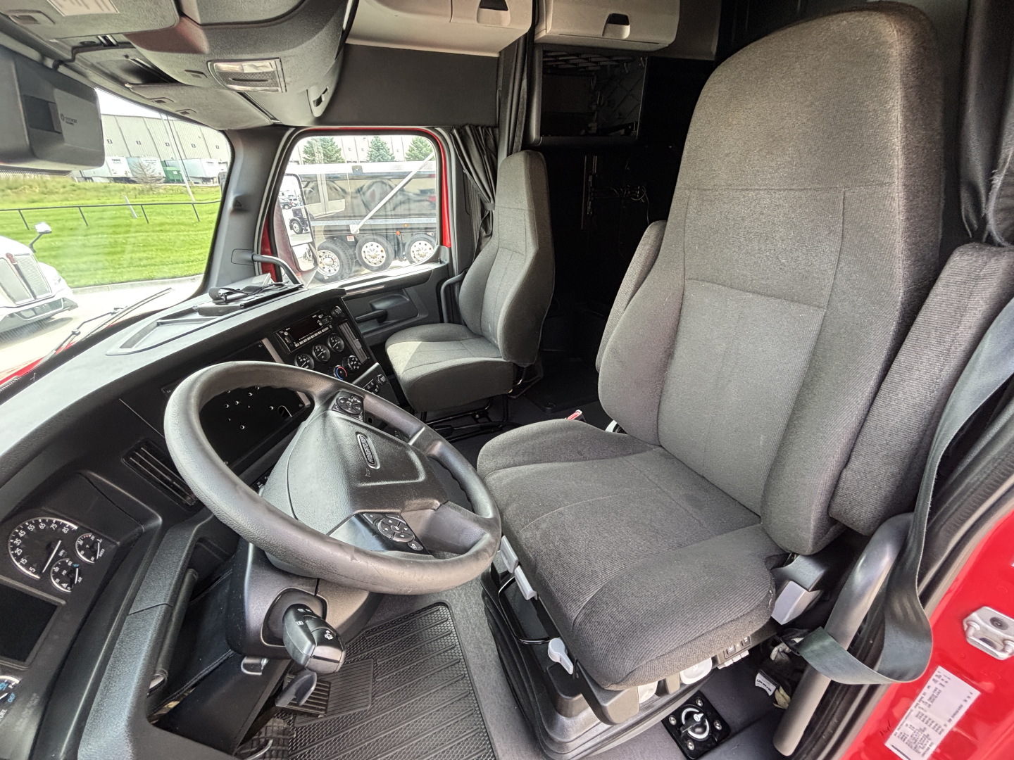 Truck cab interior showing steering wheel, driver seat, and dashboard of a Freightliner PT126064ST sleeper cab from the left-front angle.