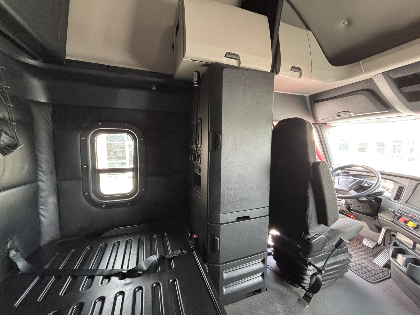 Truck cab interior showing driver seat and sleeper area with storage cabinet and window.