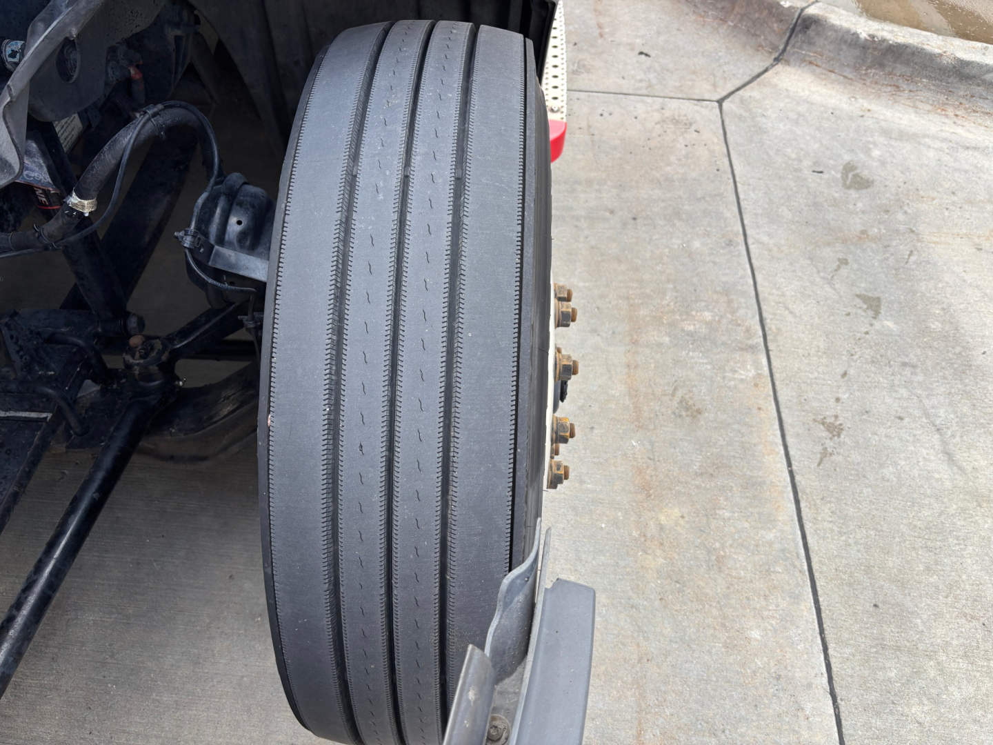 Front wheel of a Freightliner PT126064ST truck showing a single tire with grooves and wheel hub bolts visible.