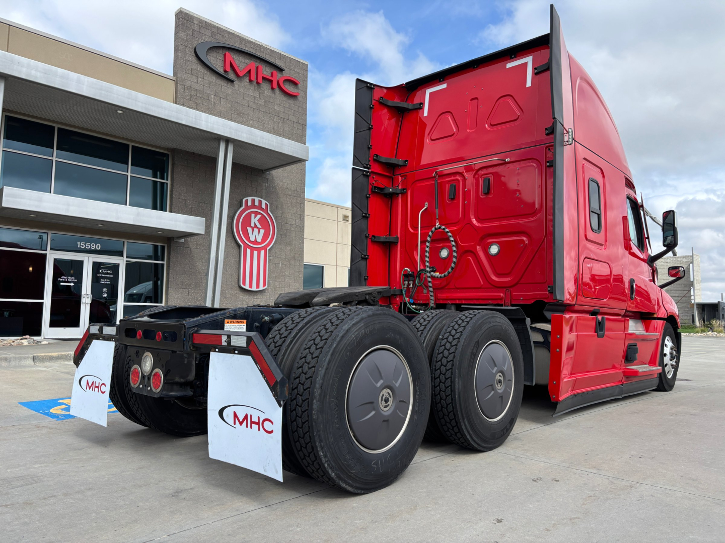 Freightliner PT126064ST truck chassis in red viewed from rear-left side showing dual rear axles, fifth wheel, and trailer hitch area at a dealership.