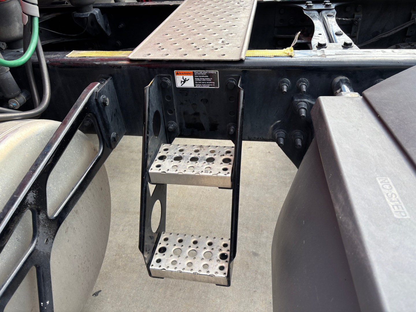 Conventional sleeper truck frame with metal steps and attachment brackets, viewed from side of chassis with perforated steel steps and surrounding components.