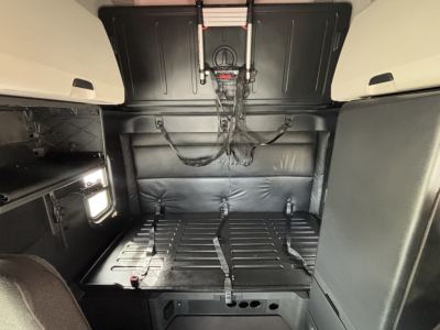 Cab interior of a Freightliner PT126064ST truck showing sleeper area with black leather-like walls and cargo floor, cab-side storage, and wiring harnesses visible.