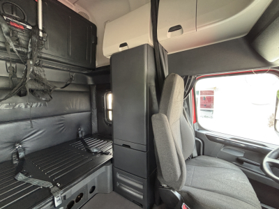 Truck cab interior showing sleeper area with bunk and wardrobe, Faced driver seat, and overhead cabinets. No visible text legible.