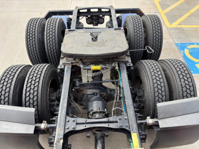 Chassis view of a Freightliner truck undercarriage showing rear axle with multiple dual tires and drive shaft components.