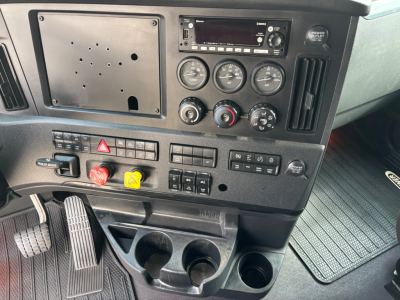 Dashboard and control panel of a Freightliner truck showing gauges, radio, and control switches; three round gauges, hazard lever, climate controls, and cup holders.