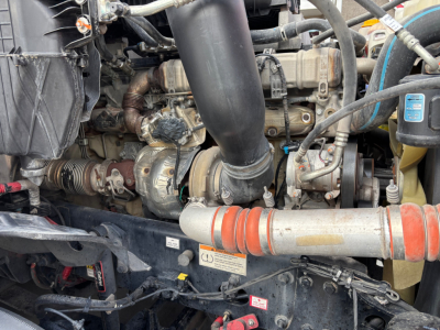 Truck engine bay showing coolant hose, turbo intake, belts, and various engine components in a Freightliner PT126064ST.