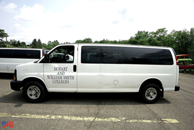White 2015 Chevrolet Express passenger van side view showing Hobart and William Smith Colleges logo.