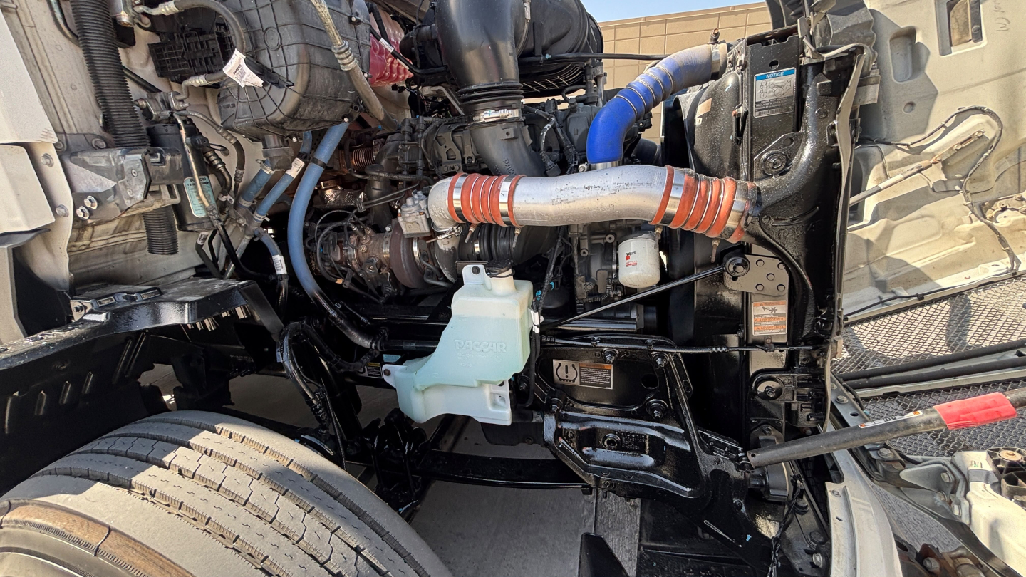 Kenworth T680 engine bay showing coolant reservoir and various hoses and belts.