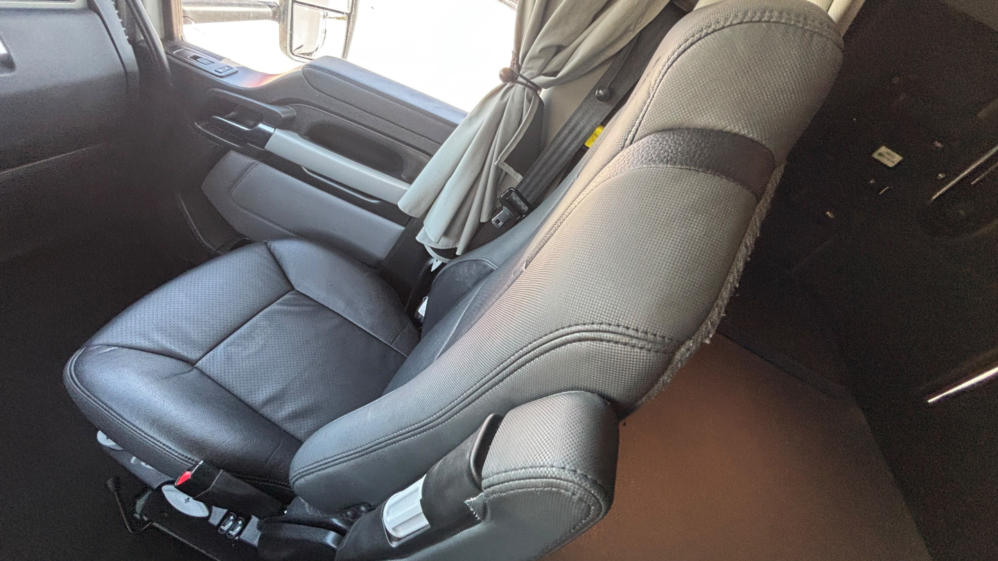 Kenworth T680 cab interior showing driver's seat and passenger seat with seat belts and dashboard.