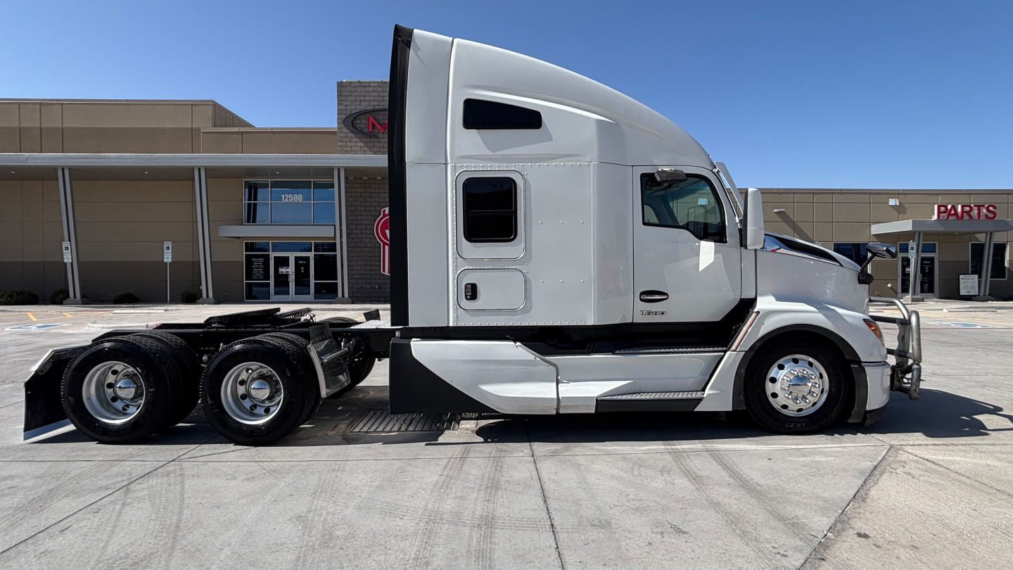 Kenworth T680 tractor side view showing sleeper cab, tandem rear axles, chrome wheels, and white exterior with side window and door details.