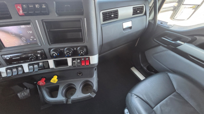 Cab interior of a 2023 Kenworth T680 truck showing dashboard controls, gear levers, and passenger seat area.